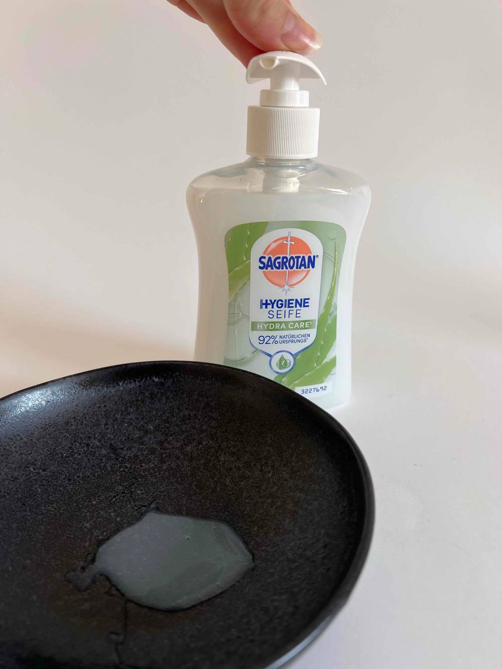 Flüssigseife getestet: Eine Hand drückt den Pumpspender einer Flasche hinter einer dunklen Schale.