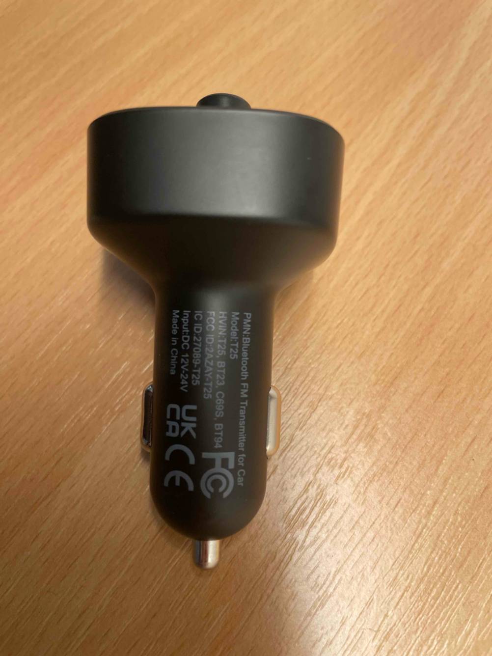 Ein schwarzer FM-Transmitter im Test inklusive Zigarettenanzünder-Adapter liegt auf einer Holzfläche.