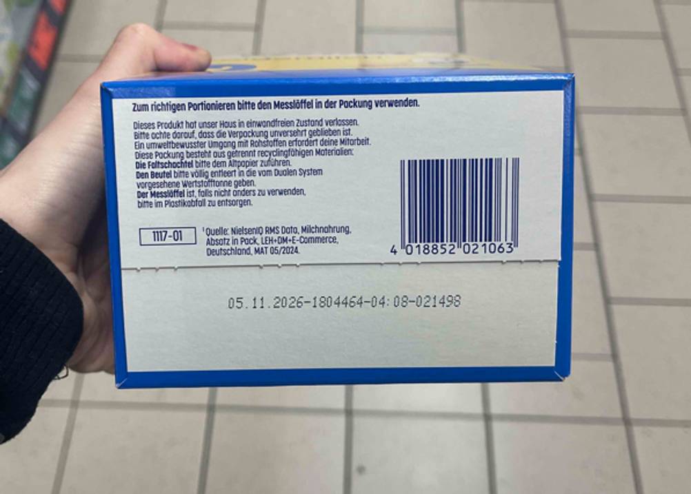 Eine Hand zeigt die Unterseite einer Packung getestete Folgemilch 2 mit Warnhinweisen.