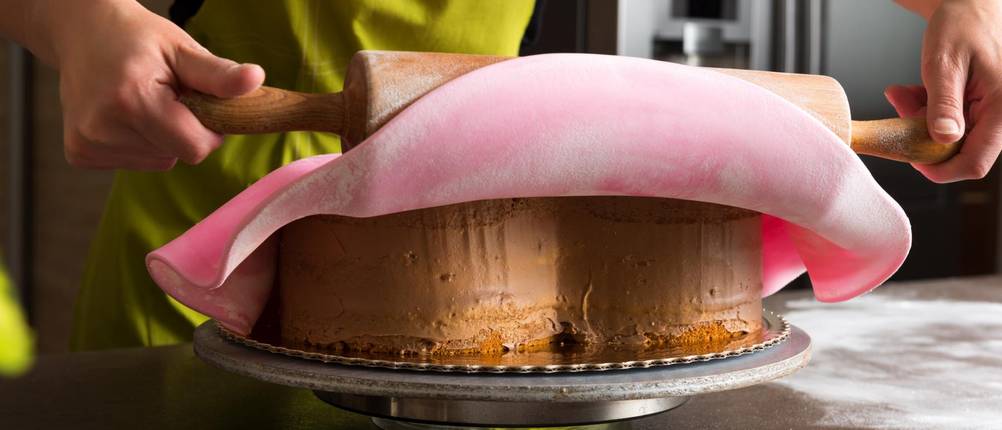 Fondant-Presse im Test: eine Frau breitet rosafarbenen Fondant mit einem Wargelholz über einen Kuchen