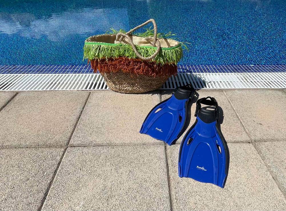 Getestete Schwimmflossen für Kinder stehen am Beckenrand vor einer trapezförmigen offenen Korbtasche.