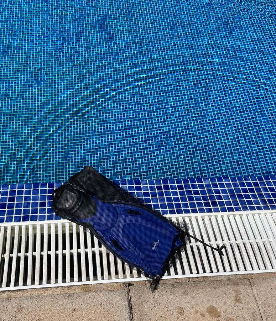 Dunkelblaue Kinder-Schwimmflossen im Test liegen innerhalb ihres schwarzen Transportnetzes am Schwimmbeckenrand.