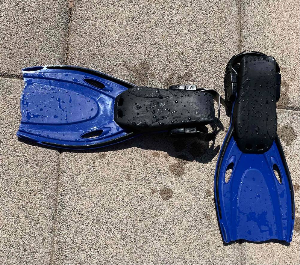 Schwimmflossen-Kinder-Test: blaue Schwimmflossen mit schwarzer Gummisohle von unten betrachtet liegen auf einem hellen Betonboden.