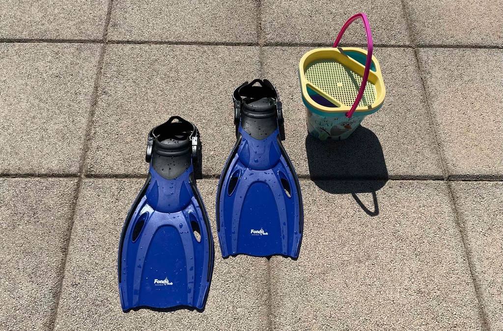 Im Test: Schwimmflossen für Kinder von Fondosub stehen neben einem Sandeimer auf Betonplatten.