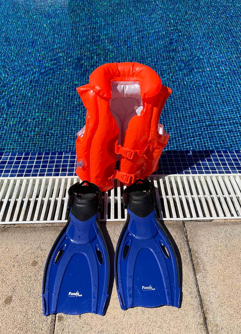 Im Test: Schwimmflossen für Kinder von Fondosub stehen vor einer aufgeblasenen Schwimmjacke am Rand eines Pools.