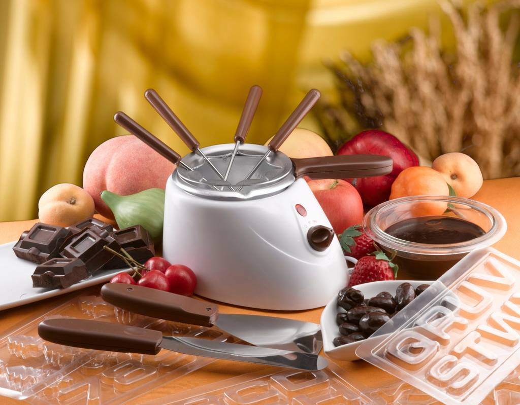 Fondue-Schokolade-Test: Auf einem Tisch stehen ein elektrisches Schokofondue und diverse Zutaten und Zubehör für das Fondue. 