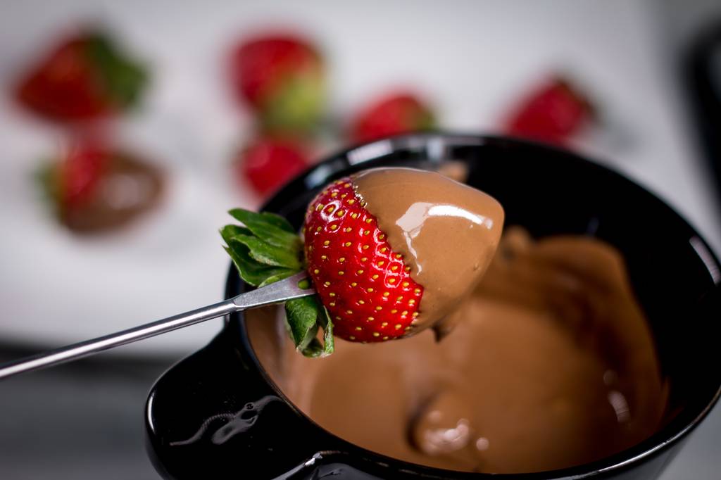 Fondue-Schokolade-Test: Eine Fonduegabel mit einer Erdbeere wird in Schoko-Fondue eingetaucht. 