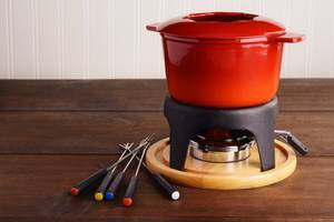Fondue-Set-Gusseisen-Test: Nahaufnahme eines roten Gusseisen-Fondues auf einem Stövchen mit fünf Fonduegabeln.