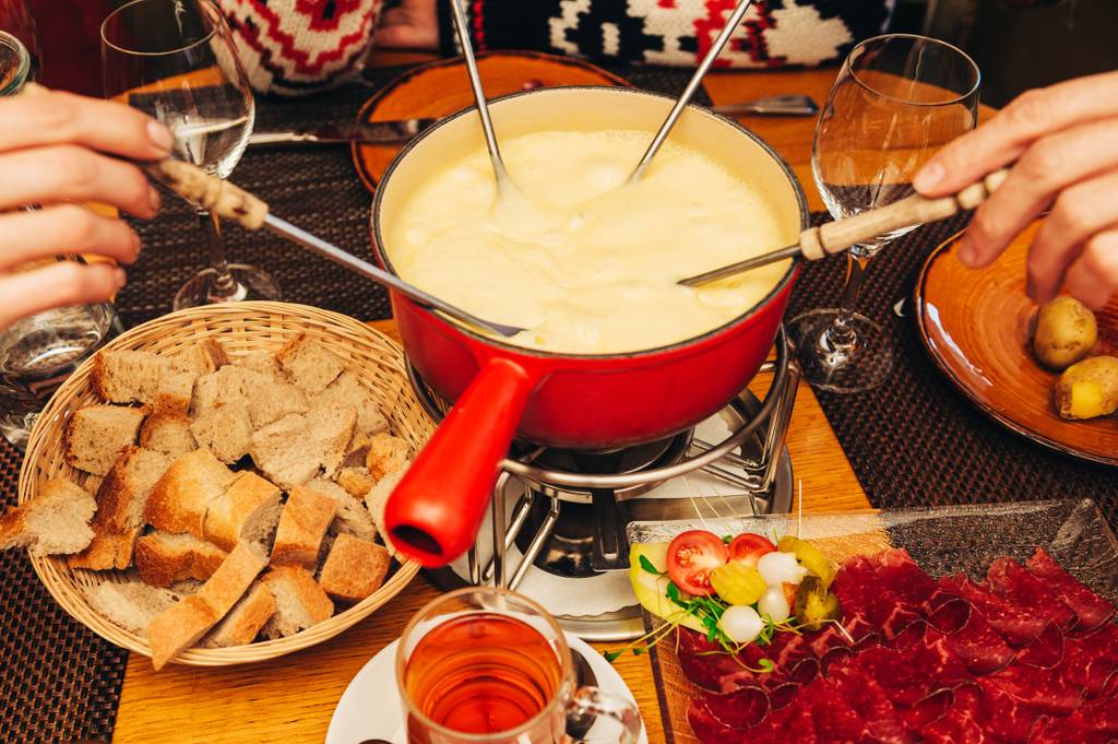 Fonduegabeln-Test: Mehrere Personen tauchen Fonduegabeln in ein cremiges Käsefondue, während rundherum verschiedene Beilagen bereitstehen.