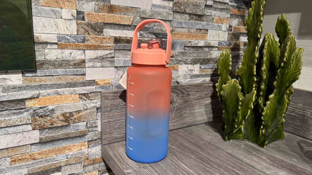 Eine Trinkflasche 2 Liter steht getestet vor einer Wand im Ziegeldesign.