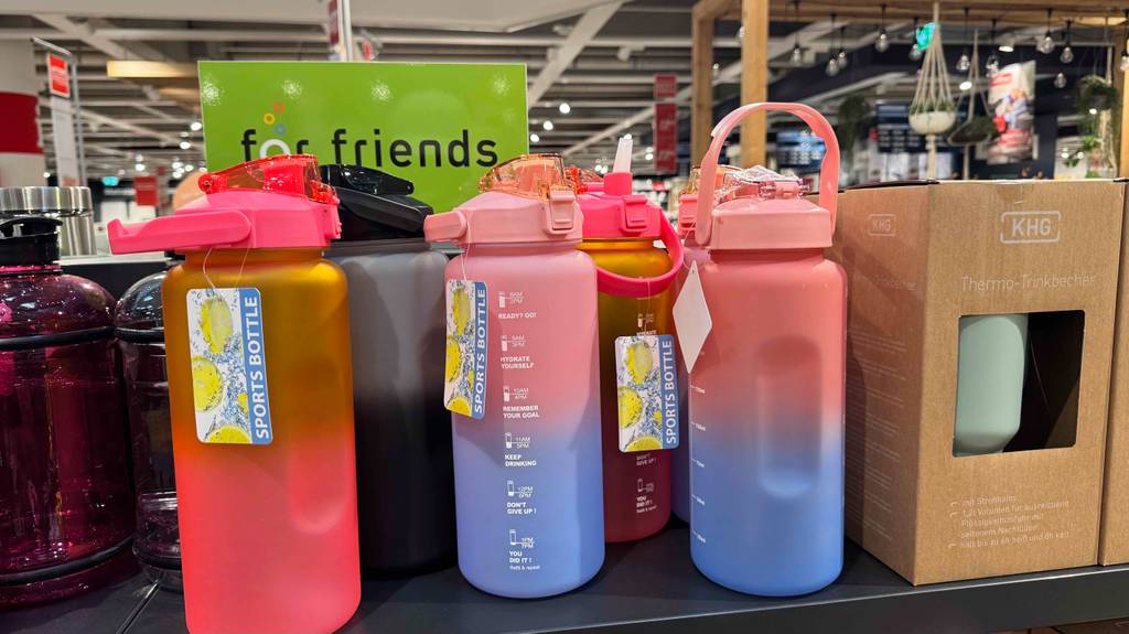 Mehrere Trinkflaschen mit 2 Liter in verschiedenen Farben und Designs stehen zum testen auf einem dunklen Regalbrett.