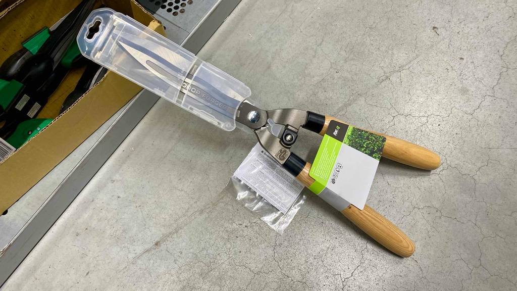 Eine getestete Hand-Heckenschere mit Holzgriff lehnt an einem Verkaufsregal.
