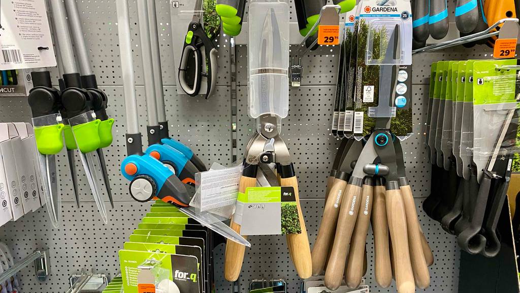 Eine Hand-Heckenschere im Test inklusive Holzgriff hängt an einem Verkaufsregal zwischen weiteren Garten-Werkzeugen.