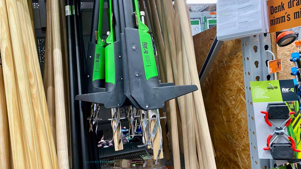 Im Test: ein Unkrautstecher in schwarz-grün, mit Fokus auf die Stechvorrichtung, hängt neben weiteren Gartenwerkzeugen in einem Geschäft.