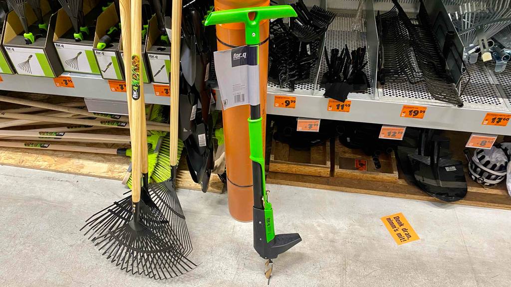Ein schwarz-grüner Unkrautstecher im Test steht neben weiteren Garten-Handgeräten vor einem Verkaufsregal für Gartenwerkzeuge.