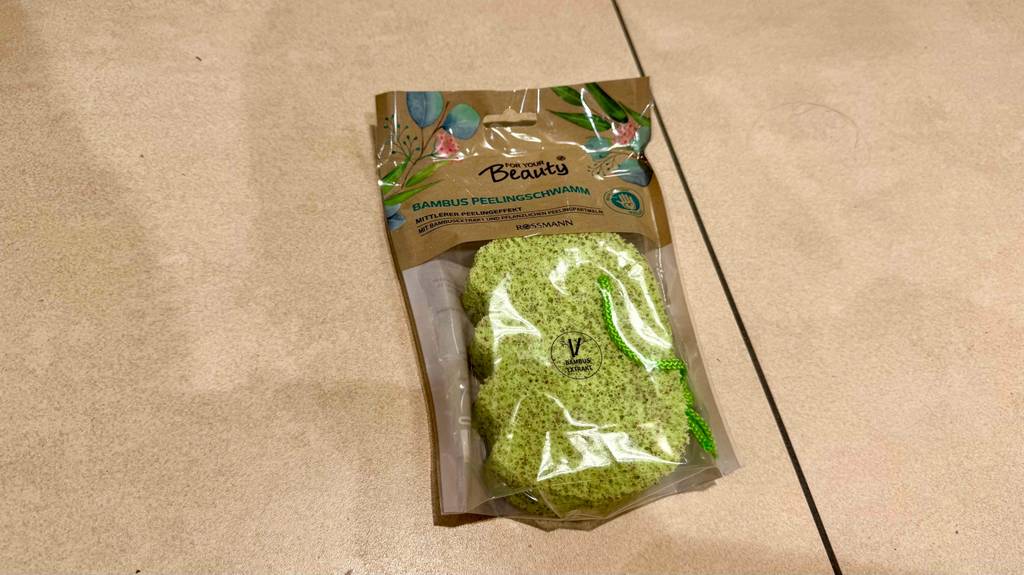 Ein verpackter Peelingschwamm liegt zum testen auf Fliesen.