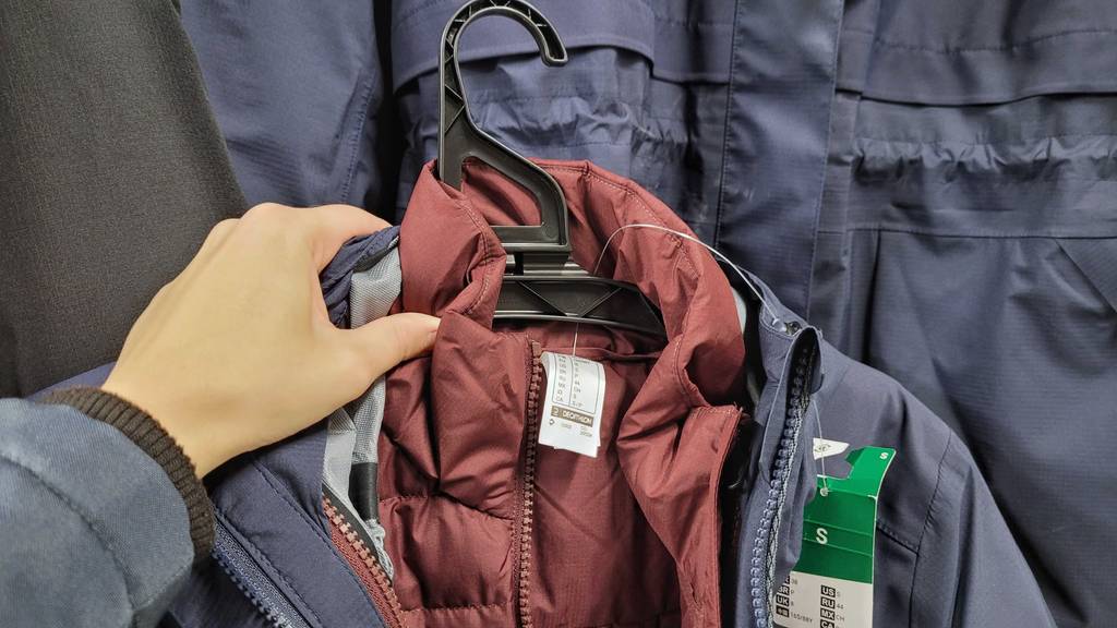 Im Test: blaue 3-in-1-Jacke inklusive rotem Innenfutter im Test wird am Bügel von einer Hand gehalten.