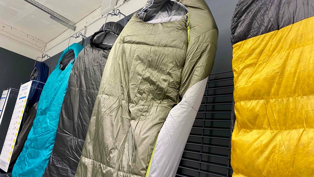 Im Test: Nahaufnahme des Kopfteils eines aufgehängten Outdoor-Schlafsacks neben anderen in einer Verkaufsausstellung.