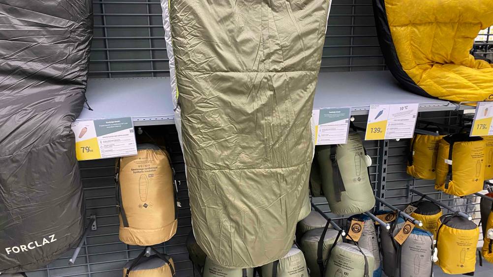 Nahaufnahme des Fußbereiches eines Outdoor-Schlafsack im Test vor einem Regal hängend mit Preisangaben und mehreren anderen Produkten unterhalb.
