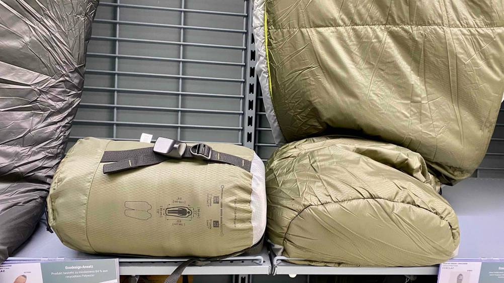 Ein originalverpackter Outdoor-Schlafsack im Test mit anderen Produkten in einem Verkaufsregal.