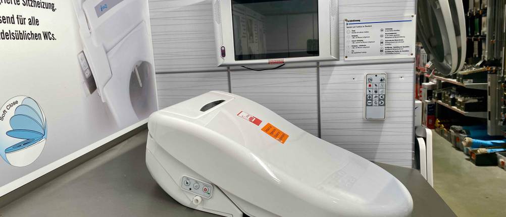 Ein Dusch-WC Aufsatz im Test von der Seite auf einer dunklen Fläche montiert.