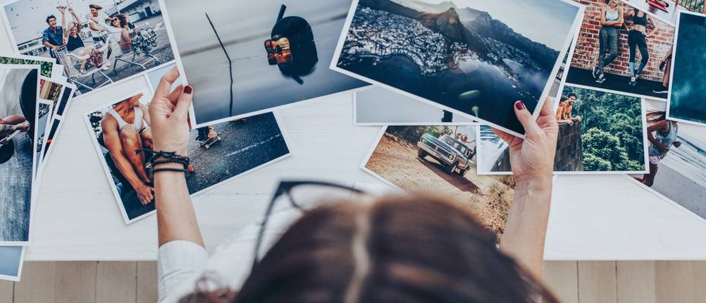 Person prüft verschiedene Fotoabzüge an einem Arbeitstisch