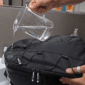 wasserdichter Fotorucksack im Test: Wasser wird mit einem Messbecher auf einen Fotorucksack geschüttet