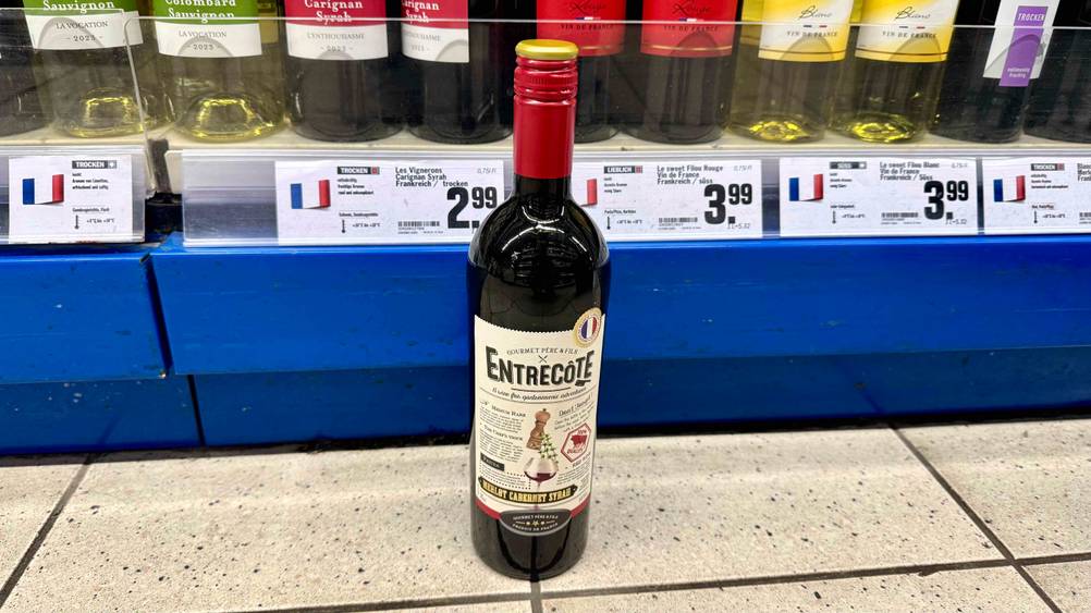 Französischer Rotwein im Test: Eine Flasche steht vor einem Verkaufsregal mit Preisangaben auf dem Boden.