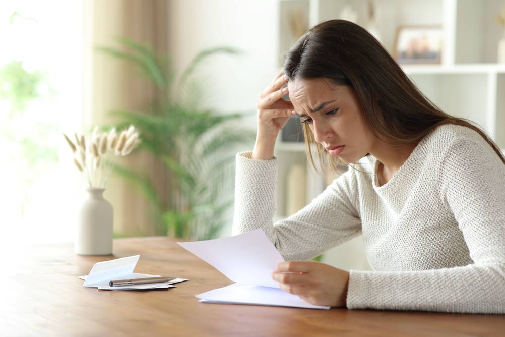 Eine Frau sitzt mit verzweifeltem Blick über mehreren geöffneten Briefen.