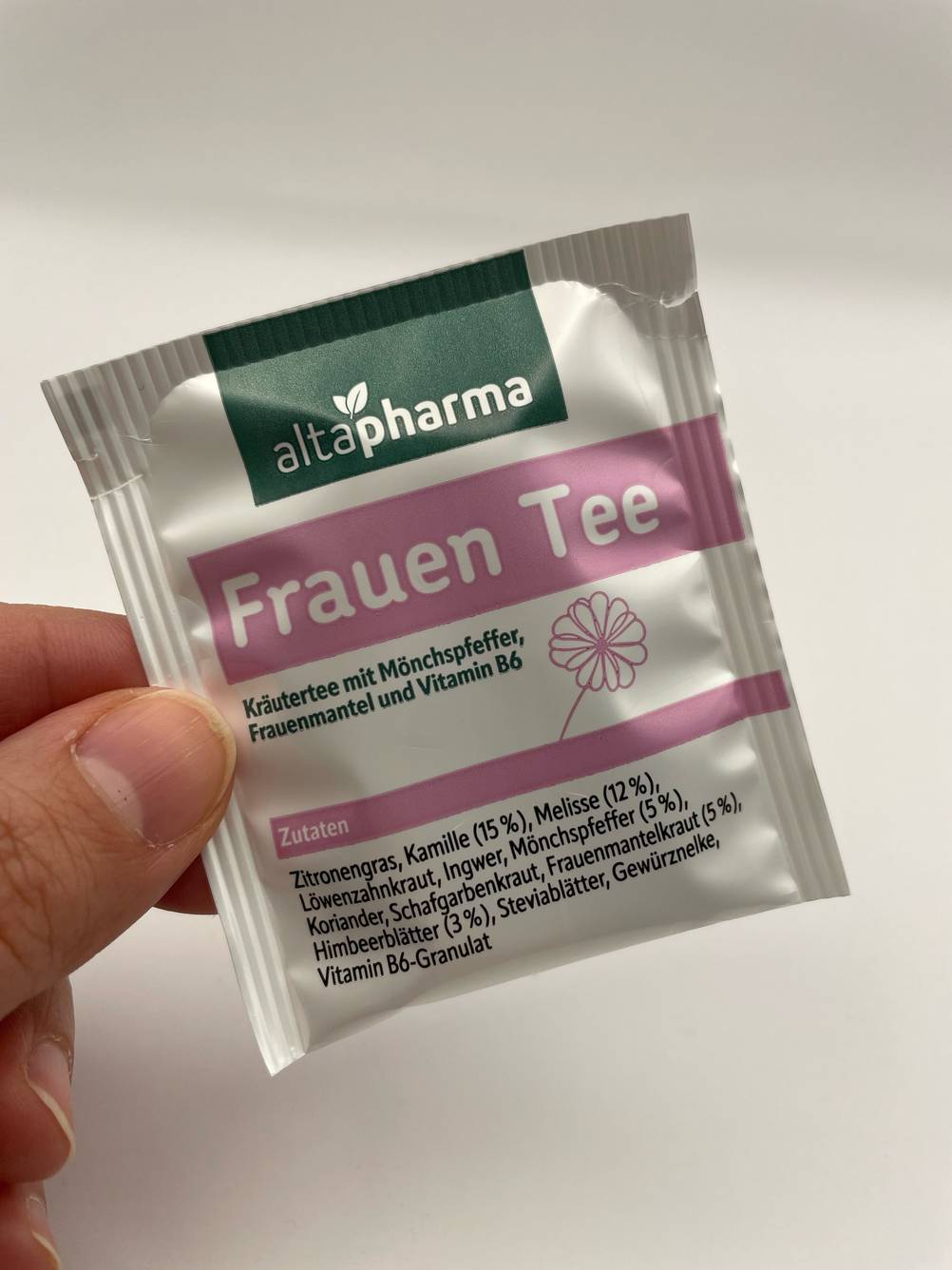 Eine Hand hält eine Einzelpackung des Frauenmanteltee im Test vor eine helle Wand.
