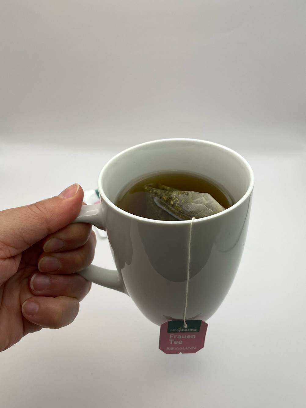 Getestet: Eine Hand hält eine Tasse mit Frauenmanteltee hoch.
