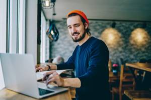 Freelance-Portale im Test: Junger Freelancer arbeitet an Laptop im Café.