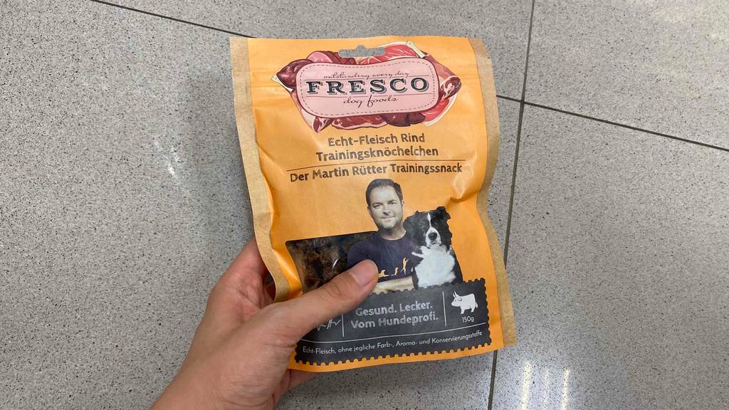 In der Hand befindet sich eine Packung getestetes Fresco-Hundefutter.