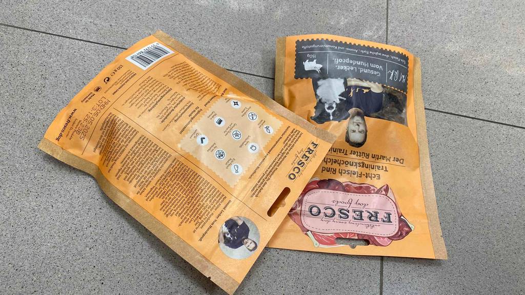 Auf dem Boden liegen zwei Packungen getestetes Fresco-Hundefutter mit Nährwertangaben. 