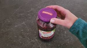 Eine Hand am violettfarbenen Deckel des Glases von Freshona, das Rotkohl im Test enthält.