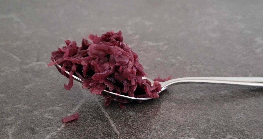 Seitenansicht auf getesteten Rotkohl auf einem Esslöffel, der sich auf einer schwarzen Oberfläche befindet.