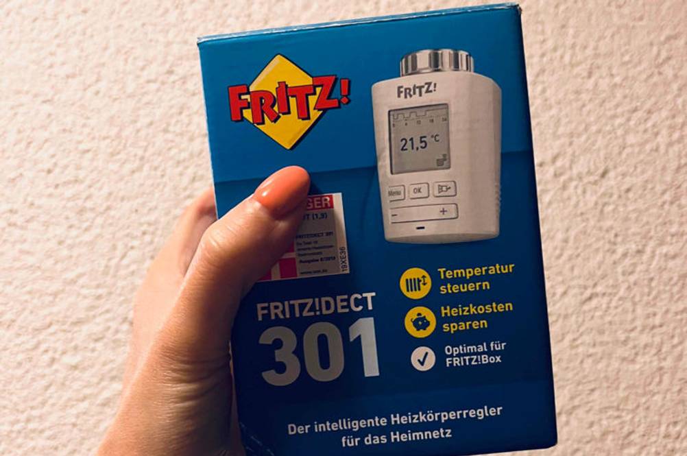 Smart-Home-Heizkörperthermostat getestet: Hand hält die Verpackungsschachtel von einem Fritz-Smart-Home-Heizkörperthermostat vor weißer Wand.