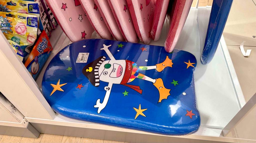 Bodyboard für Kinder getestet: Blick von oben auf ein blaues Board mit lustigem Design, das vor mehreren stehenden liegt.