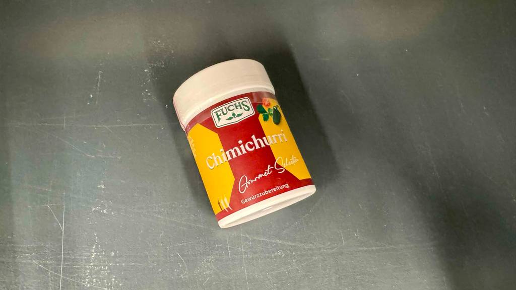 Ein getestetes Chimichurri-Gewürz in der Dose der Marke Fuchs liegt auf einer grauen Oberfläche.