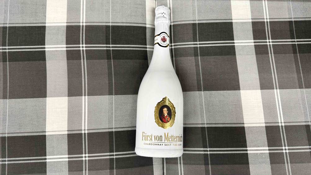 Eine Flasche des getesteten Fürst-von-Metternich-Sekts liegt auf einer karierten Fläche.