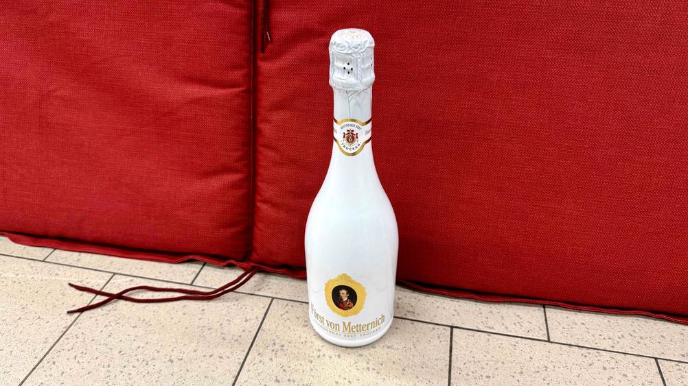 Vor einem roten Polster steht der getestete Fürst-von-Metternich-Sekt auf dem Boden.