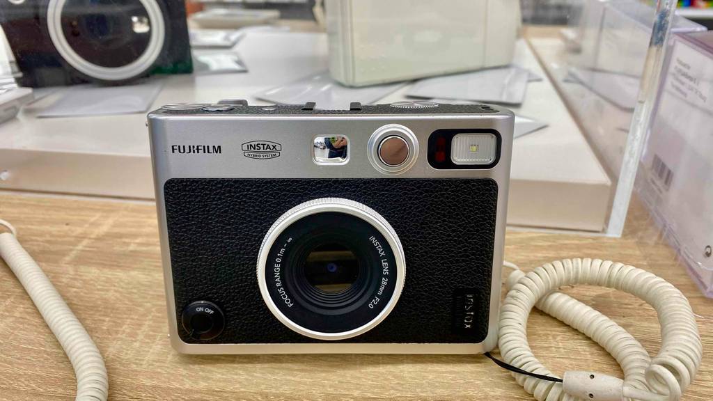 Nahaufnahme von vorn einer Fujifilm Instax Sofortbildkamera im Test, die über einen integrierten Blitz verfügt und in einem Verkaufsbereich steht.