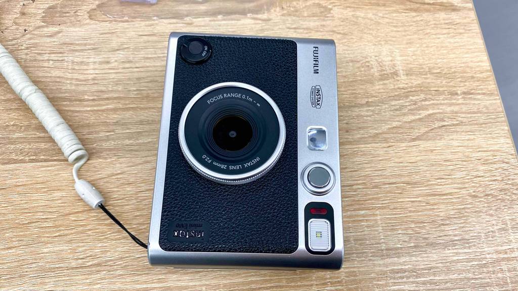 Ansicht von oben auf eine schwarz-silberne, getestete Sofortbildkamera von Fujifilm, mit Fokus auf die Linse inklusive Focus Range von 0,1 m bis ins Unendliche..