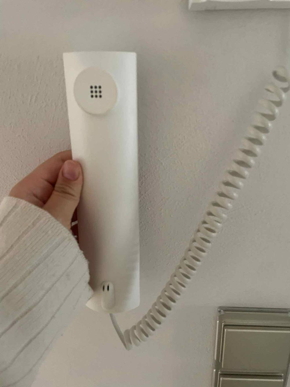 Eine Hand hält den Hörer einer getesteten Funk-Video-Türsprechanlage vor eine helle Wand.