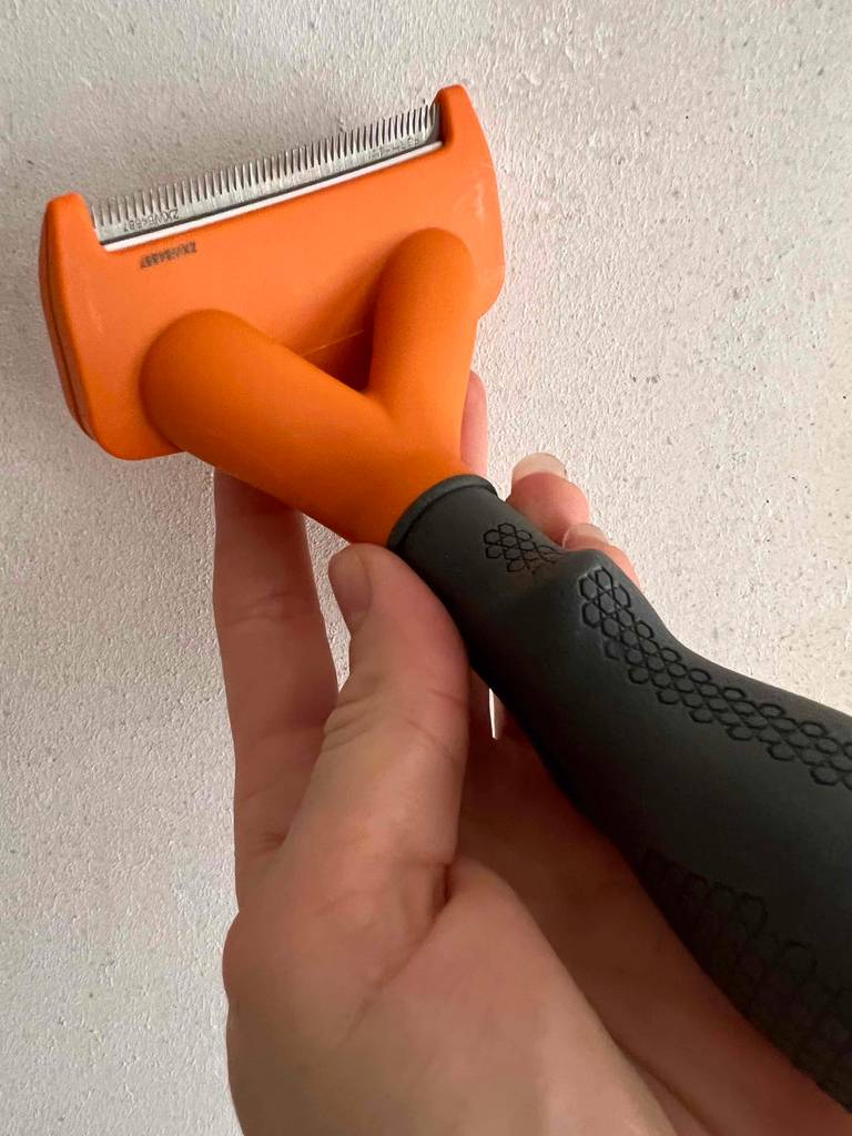Hundebürsten-Test: Eine Hand hält ein Exemplar mit der Klinge vor einer weißen Fläche.