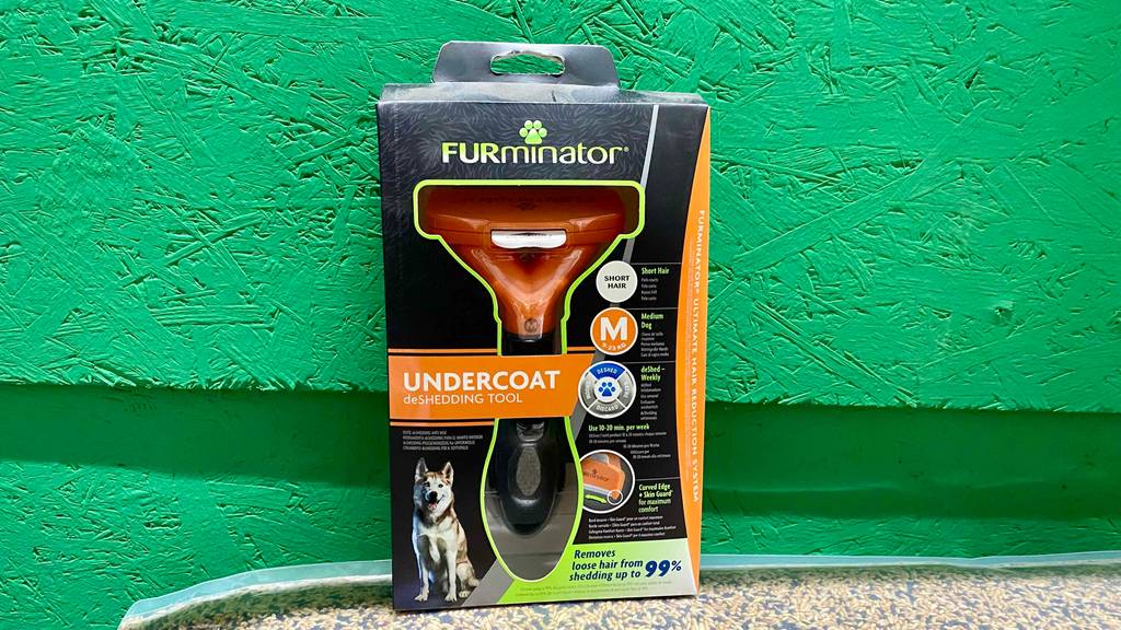 Hundescheren-Test: eine schwarze Packung mit einem Undercoat Hunderasierer lehnt an einer grünen Wand.