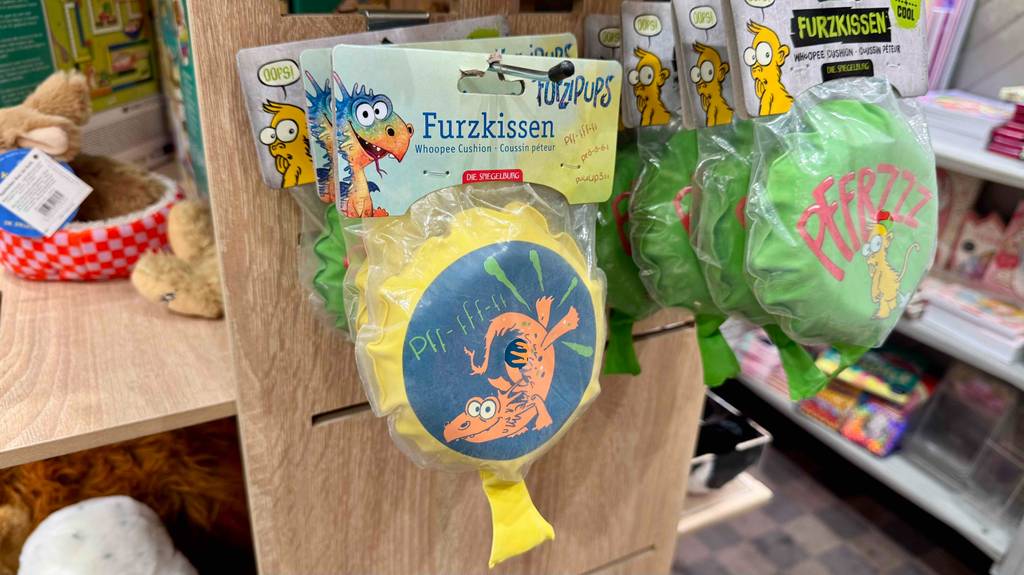 Das mit Drachenmotiv bedruckte Furzkissen im Test hängt in Zellophan eingepackt an einem Verkaufsstand mit Spielzeug.