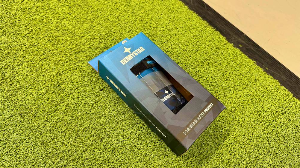 Auf einem Kunstrasen liegen die verpackten Fußball-Schienbeinschoner im Test.