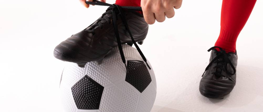 Fußballschuhe-Herren-Test: Mann bindet schwarzen Fußballschuh auf Fußball.