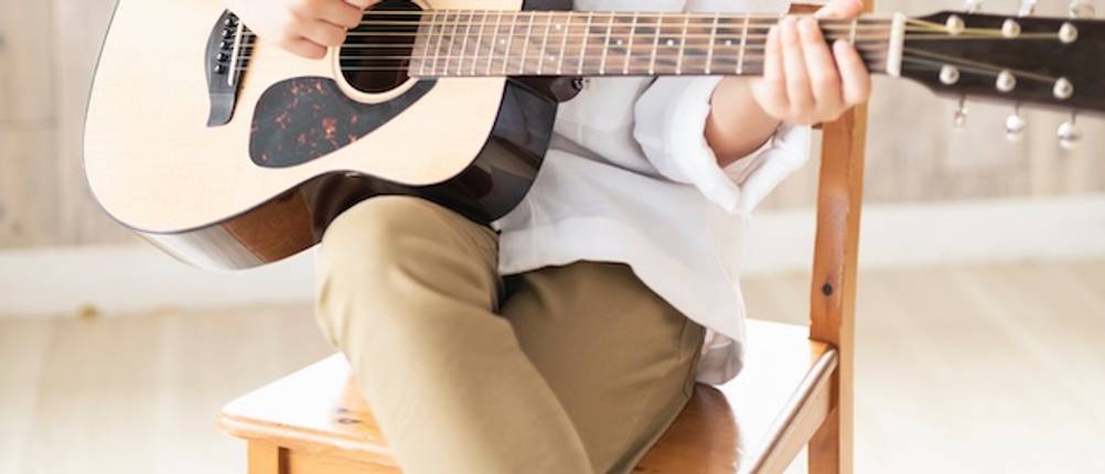 Ohne Fussbank die Gitarre getestet: Eine Gitarre wird mit zwei übereinander geschlagenen Beinen gespielt.